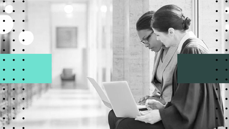 Two judges sitting in the hall of a courtroom, collaborating on their laptops