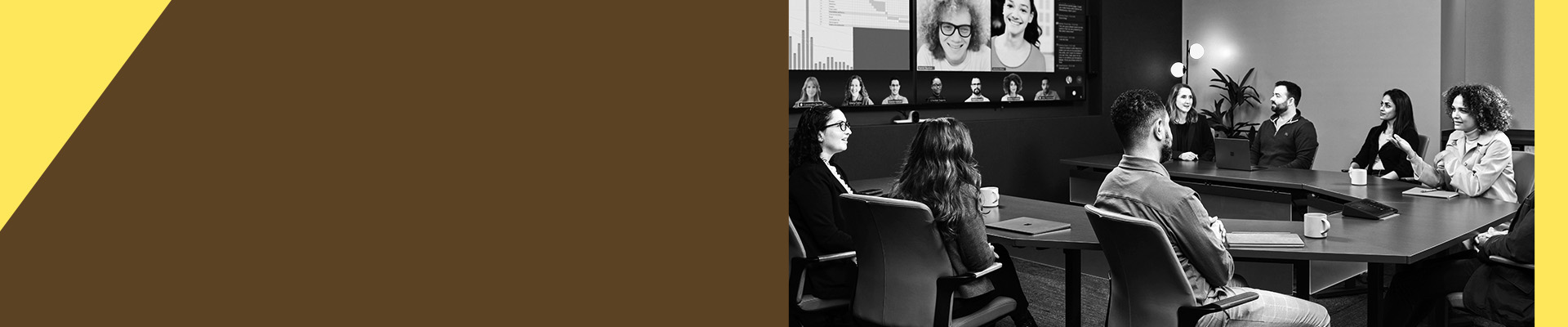 A conference room with people seated at a table, participating in a video conference displayed on large screens.