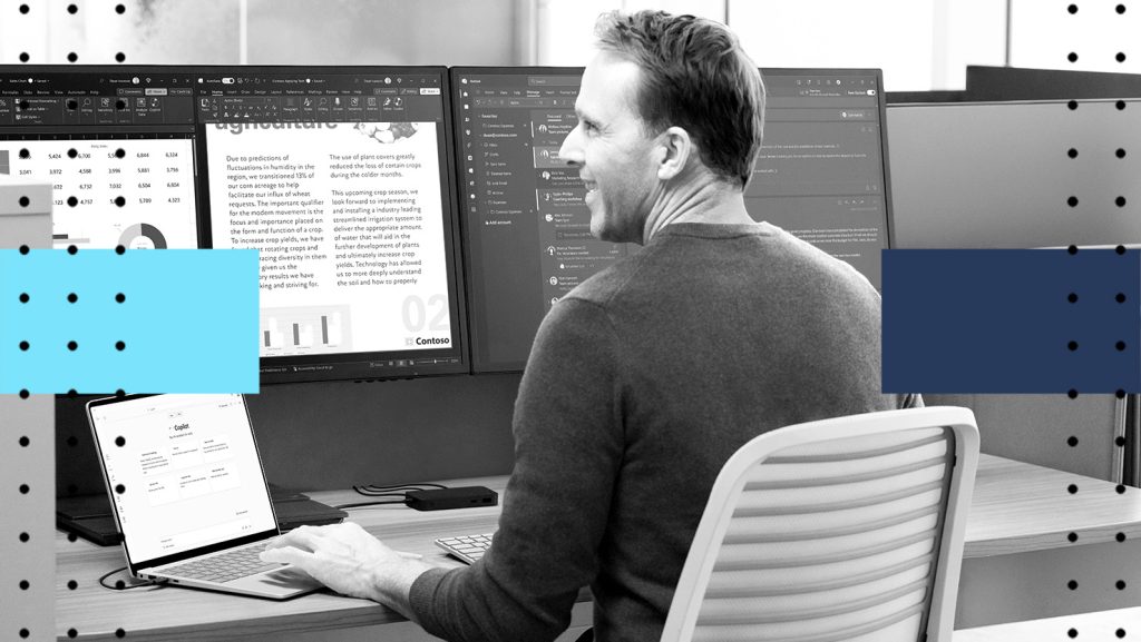 A man sitting at a desk in front of multiple computer monitors using a laptop