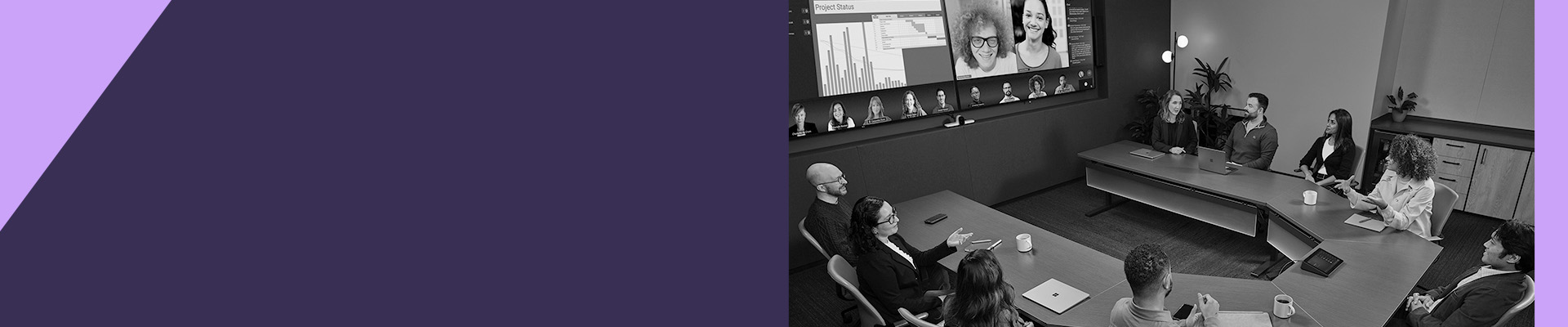 A group of people sit around a conference table in a modern meeting room while viewing remote participants on a large video screen.